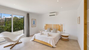 Une chambre moderne avec un lit, des tables de chevet, une chaise et une vue dégagée grâce à de grandes fenêtres.