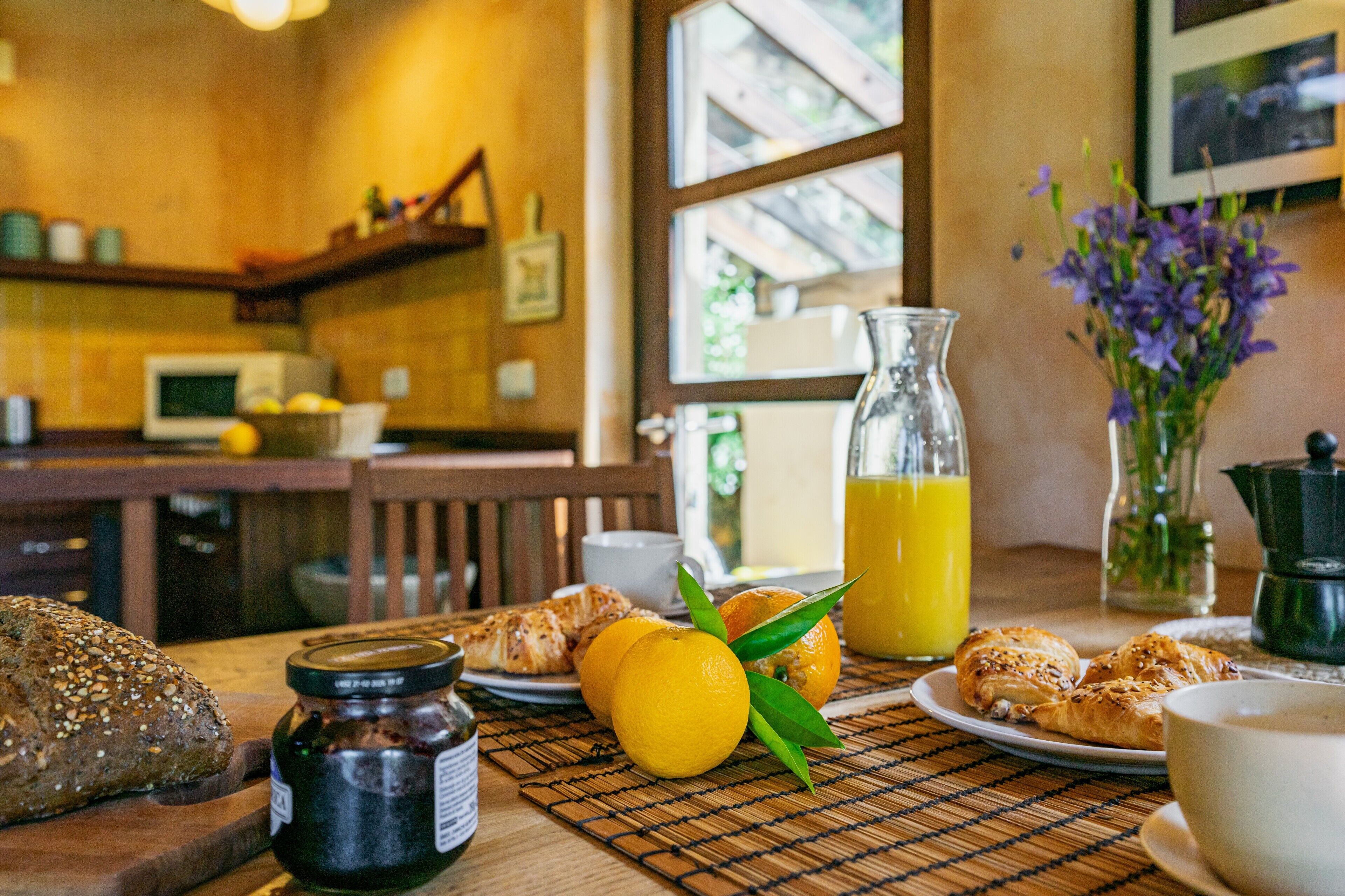 En frukostuppsättning med bröd, bakverk, apelsiner och en kanna apelsinjuice på ett bord.