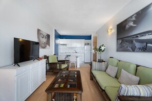 A living room with a television, sofa, coffee table, and kitchen in the background.