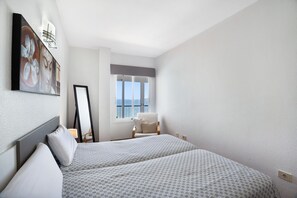 A hotel room with two beds, a large window with a view, a chair, and a painting on the wall.