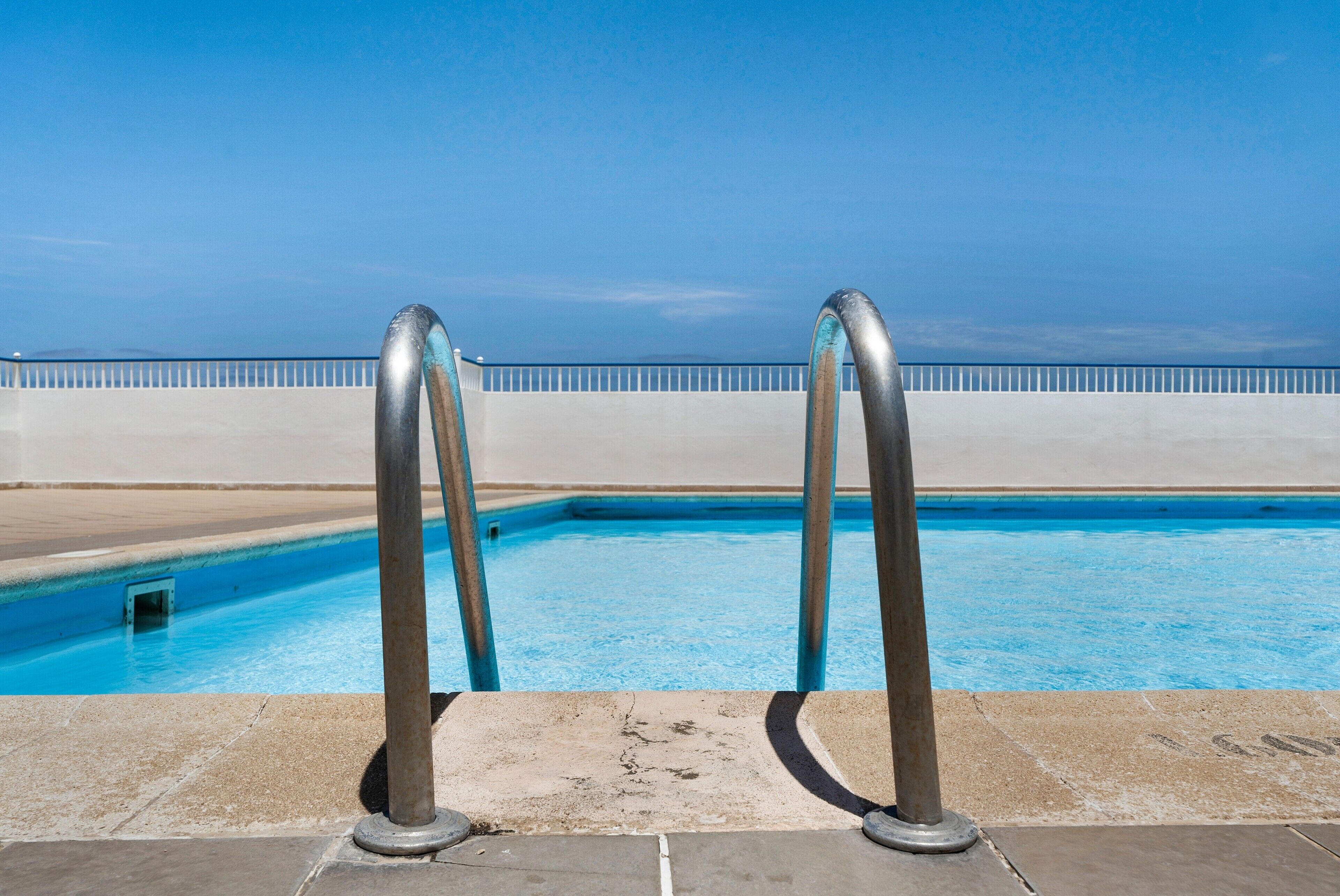 A swimming pool with metal railings and a clear blue sky.