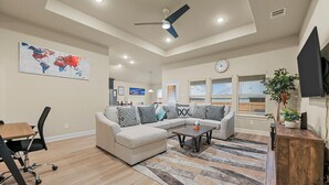 A modern living room with a sectional sofa, a coffee table, a desk with a chair, and a world map on the wall. - Entire Home in Denton, Texas. Centrally Located! Luxurious Home Away from Home! (Denton)