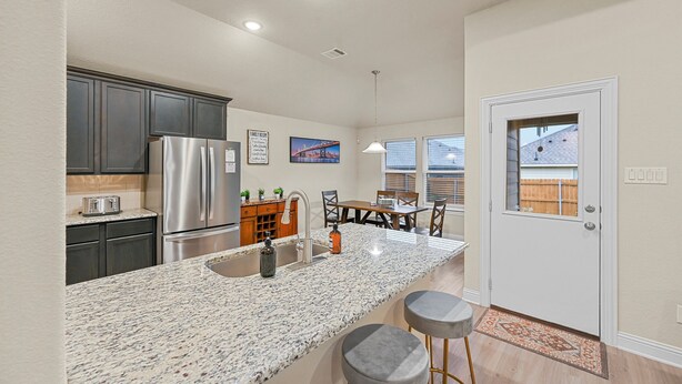 A modern kitchen with granite countertops, stainless steel appliances, and a dining area with a table and chairs. - Entire Home in Denton, Texas. Centrally Located! Luxurious Home Away from Home! (Denton)