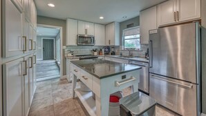 Una cocina moderna con electrodomésticos de acero inoxidable, armarios blancos y una isla grande con cubierta de vidrio.