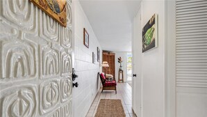 Un couloir avec un mur orné de motifs, une porte, une chaise et une plante.