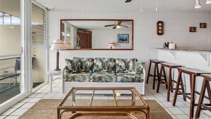 Un salon comprenant un canapé, une table basse, un ventilateur de plafond, un coin bar et un grand miroir.