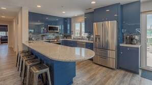 Une cuisine moderne avec des meubles bleus, des appareils en acier inoxydable et un grand îlot central doté de tabourets de bar.