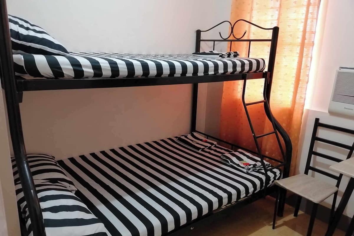 A bunk bed with black and white striped bedding, a table with a chair, and an air conditioning unit on the wall.