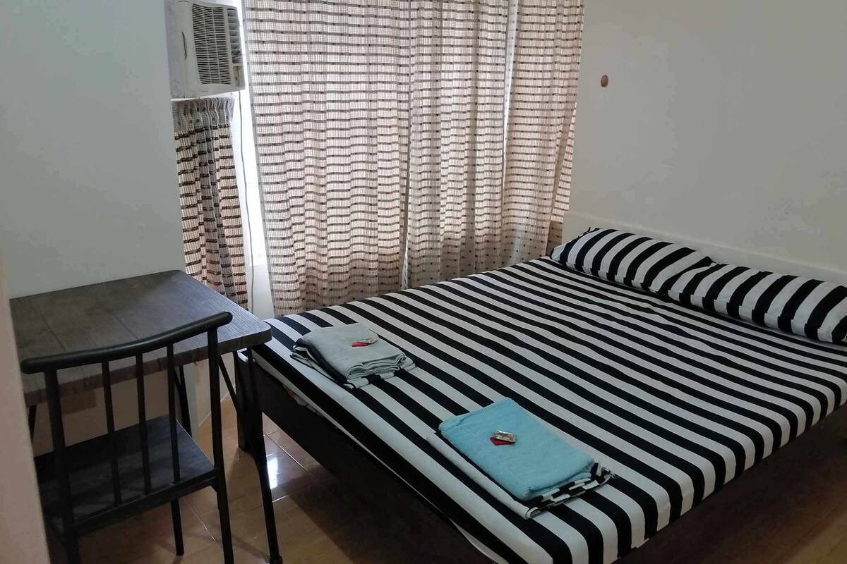 A room with a bed, a desk, and an air conditioning unit.