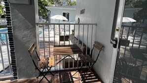 Un espace extérieur abrité avec une table et des chaises, une piscine en arrière-plan et une porte donnant sur un autre espace.
