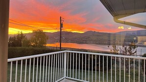 A balcony with a view of a sunset over a lake and hills. - Relax on the deck and enjoy the beautiful lake views in Vernon, (North Okanagan) (Vernon)
