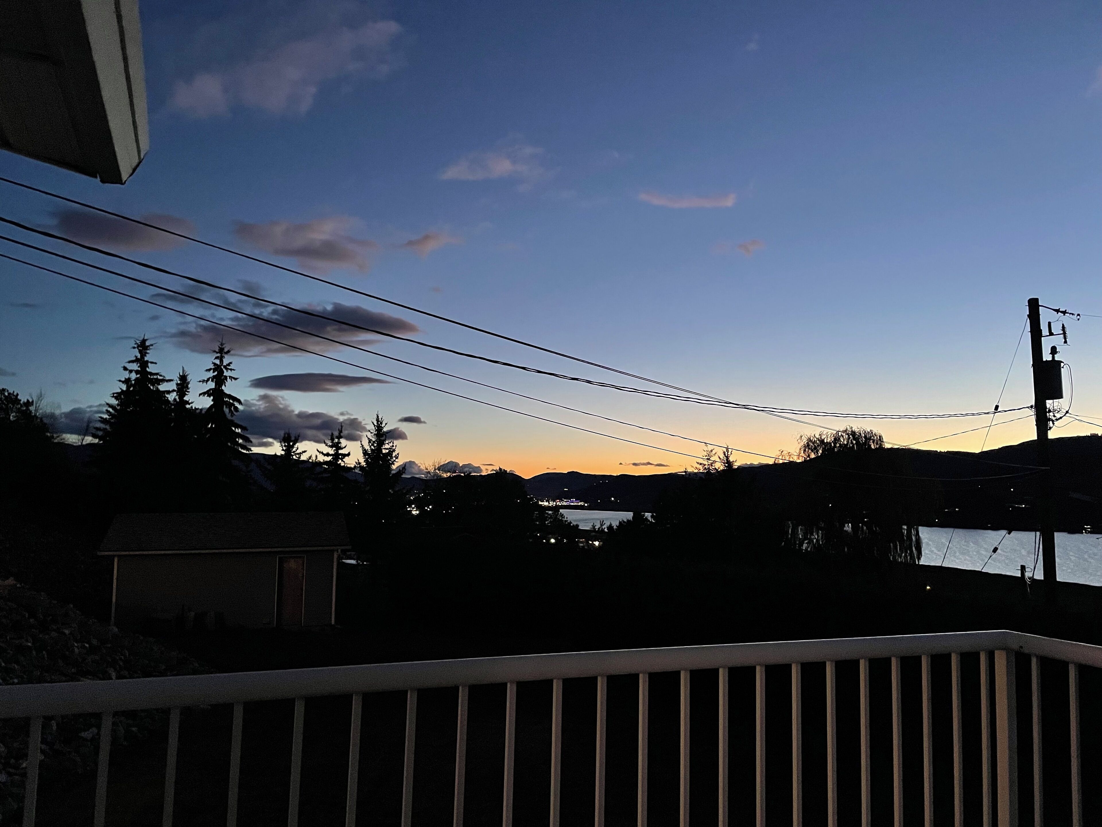 A balcony with a view of a sunset over a body of water, surrounded by trees and a distant mountain range.