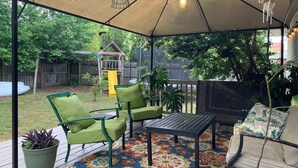 A covered patio with a table and chairs, a colorful rug, and a play structure in the background. - Please do not book (Augusta)