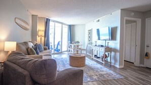 Una sala de estar moderna con un sofá, una mesita de centro y un televisor. Hay un comedor con una mesa y sillas.