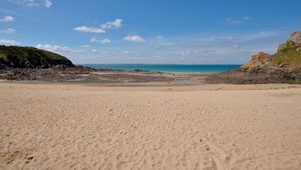 Ein sandiger Strand mit felsigen Klippen und einem klaren, blauen Himmel.