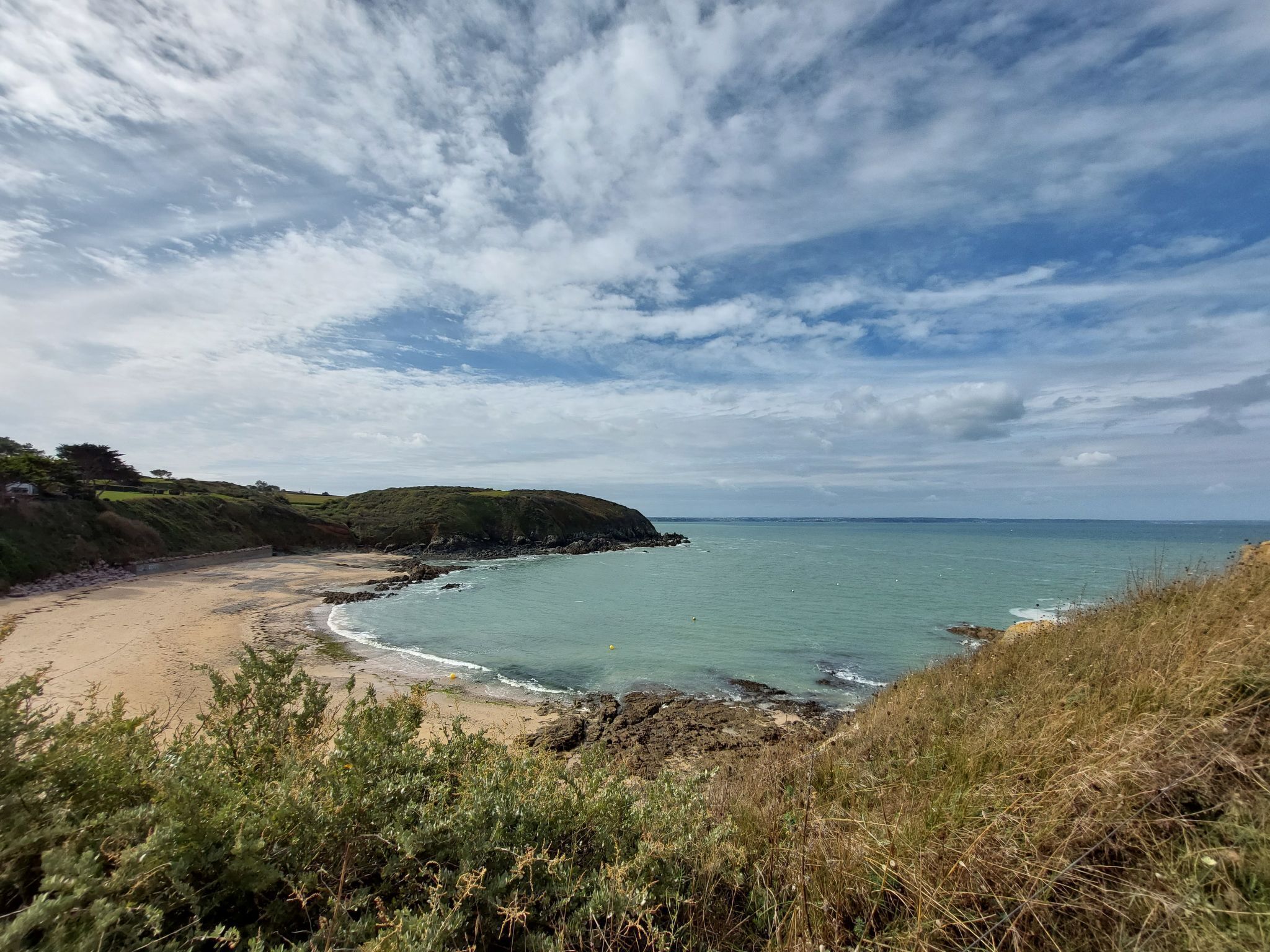A coastal landscape with a sandy beach, rocky shoreline, and grassy hills.