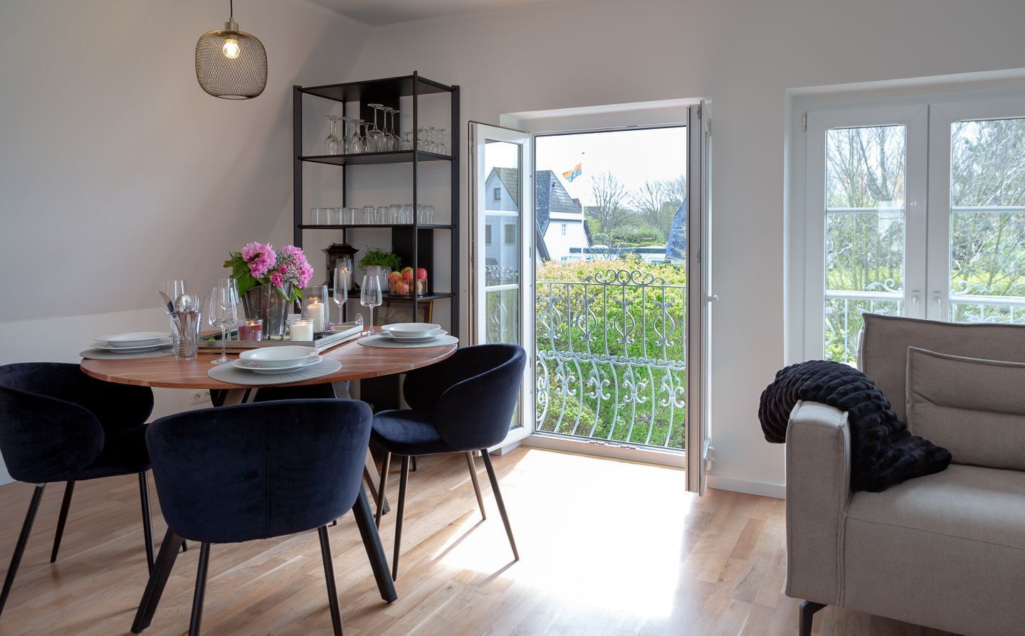 Un coin repas comprenant une table ronde, des chaises foncées, un buffet en verre contenant de la verrerie, et un balcon doté d’une rambarde en métal.
