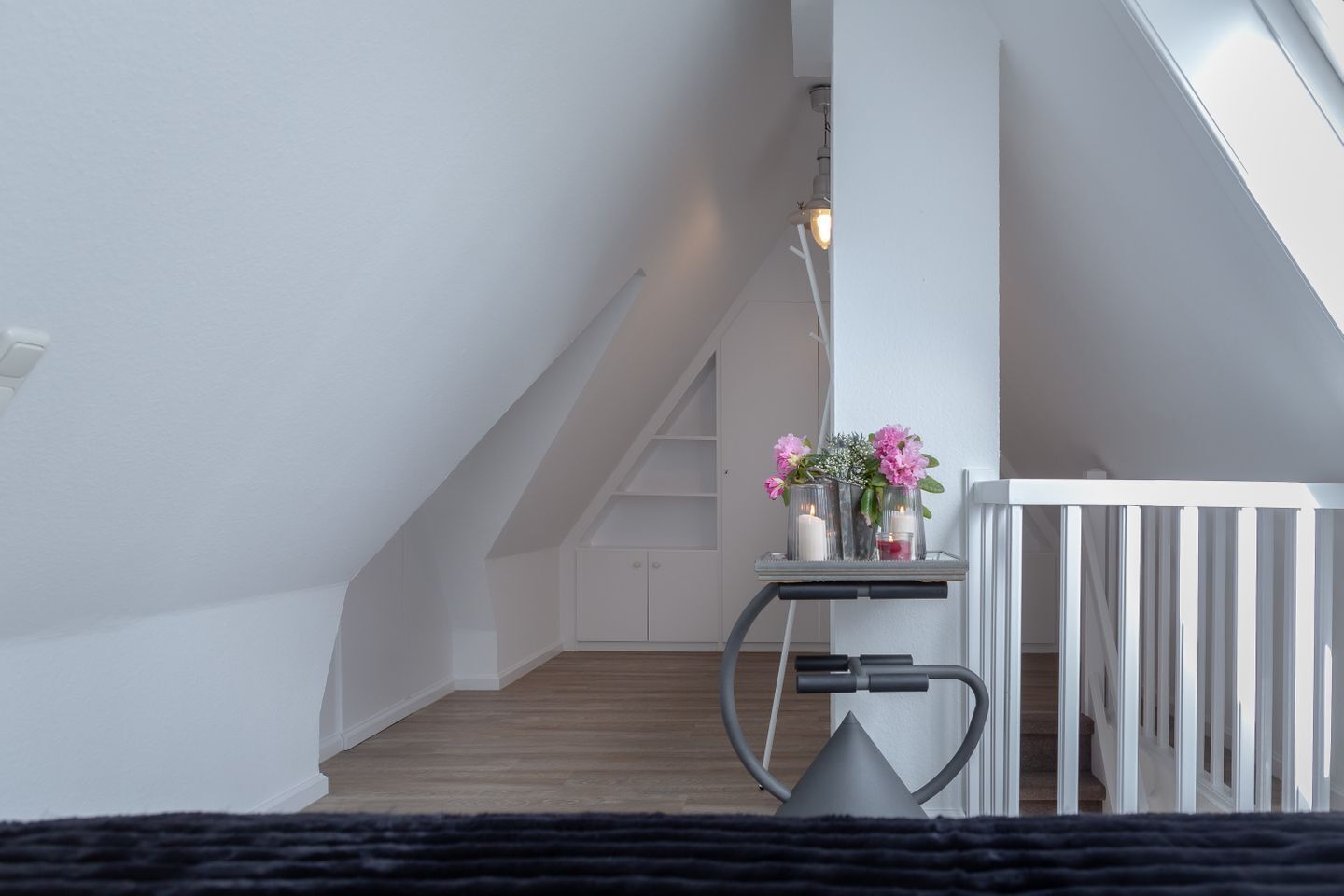 A modern, minimalist room with a sloped ceiling, a small table with candles and flowers, and a radiator.