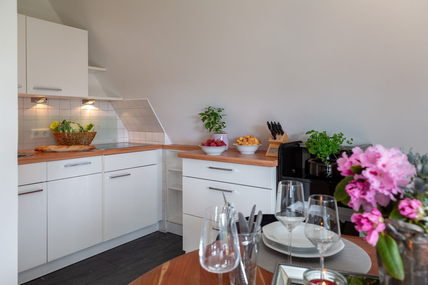 Una cocina moderna con armarios blancos, encimera de madera y zona de comedor lista para una comida.