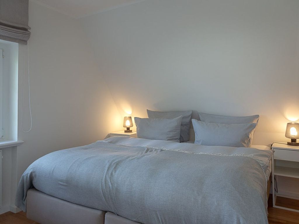 A bedroom with a large bed, two bedside lamps, and a nightstand.