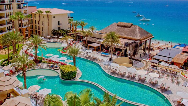 Un resort con una gran piscina, palmeras y vistas al océano.