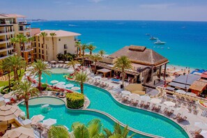 A resort with a large swimming pool, palm trees, and a view of the ocean.