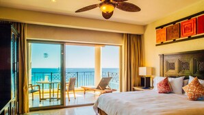 Habitación de hotel con una cama grande, un balcón con mesa y sillas, y vista al océano.