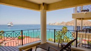 Un balcón con vista al mar y un crucero, con una mesa y sillas.