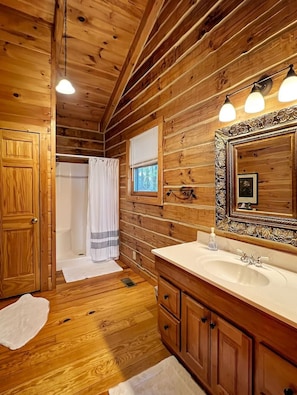 A wooden cabin bathroom with a sink, mirror, and shower.