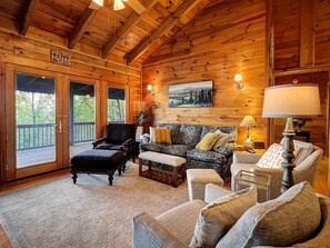A cozy cabin interior with a wooden ceiling, a sofa set, a chair, a bench, and a painting on the wall.