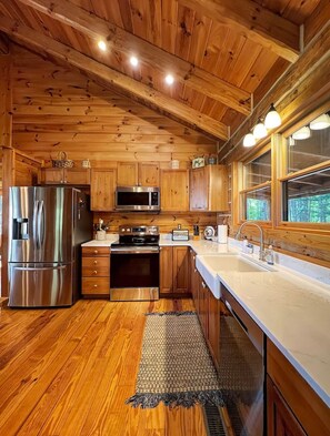 A wooden cabin interior with a kitchen featuring a refrigerator, microwave, stove, and sink.