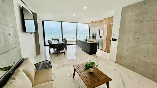 Un moderno salón con una ventana grande con vistas al mar, un comedor y una cocina.