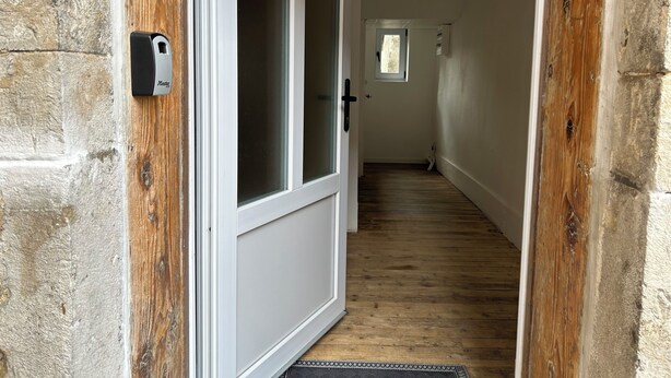 Un pasillo estrecho con suelo de madera y una puerta blanca con un panel de vidrio satinado.
