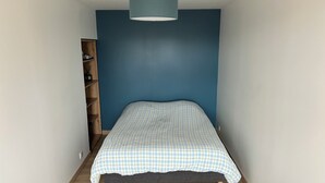 Un dormitorio con una cama, pared azul, suelo de madera y una lámpara colgante.