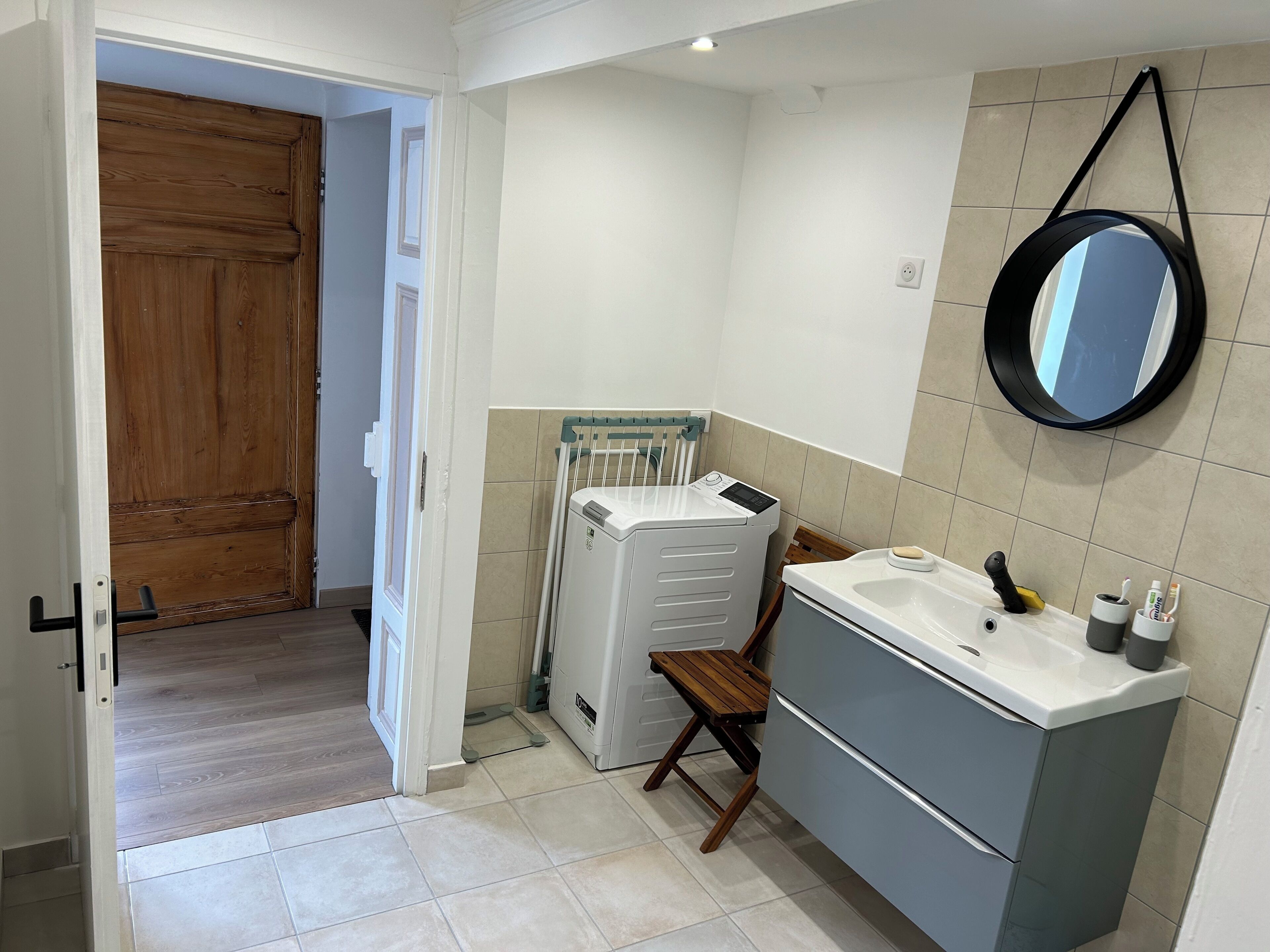 Une salle de bain avec une porte en bois, un lave-linge, un évier, un miroir et une chaise.
