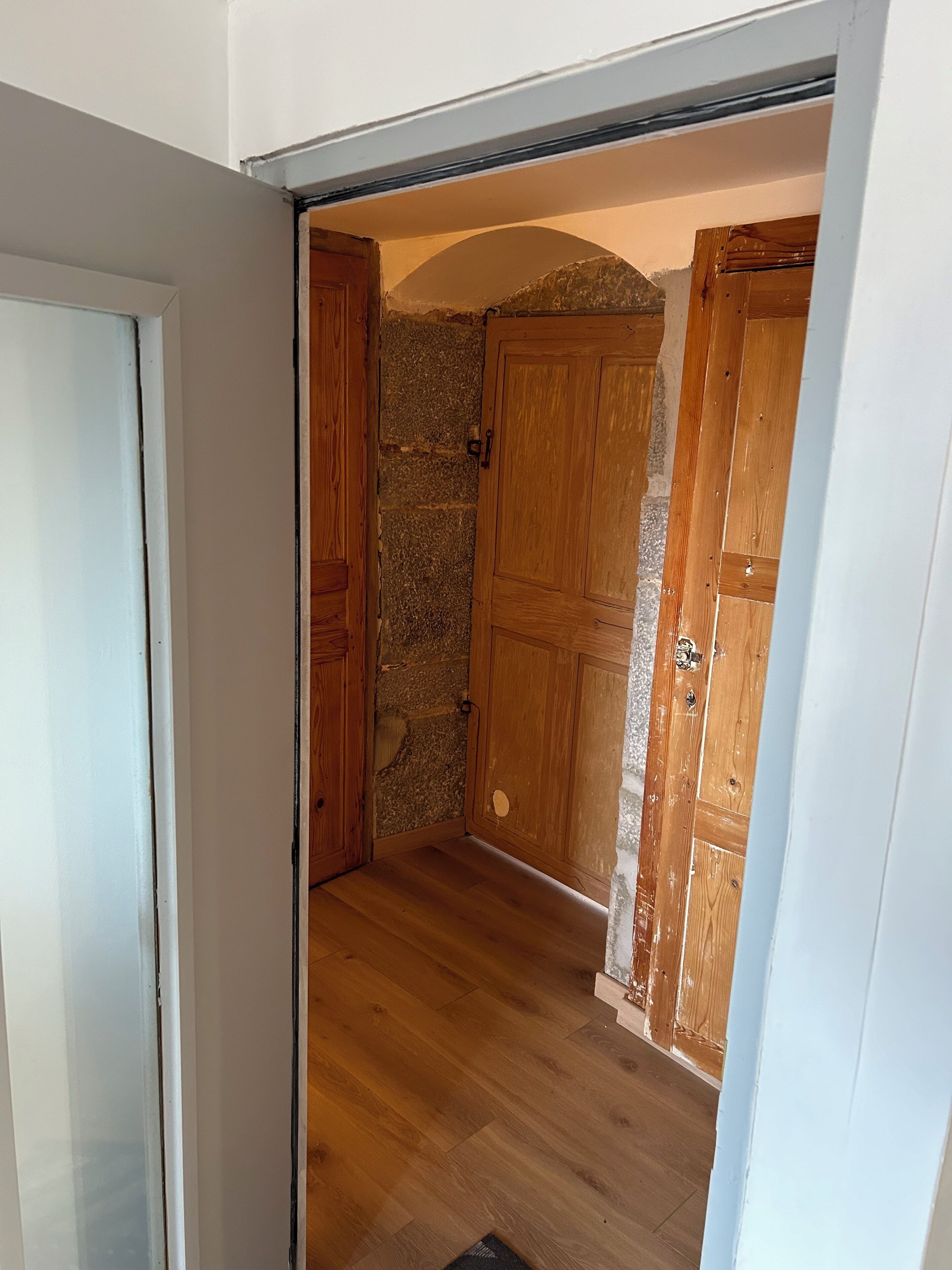Un couloir étroit avec des portes en bois et un mur en pierre.