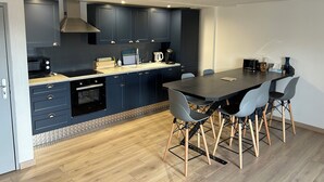 Una cocina moderna con armarios azul oscuro, una encimera de madera y un comedor con mesa negra y sillas grises.