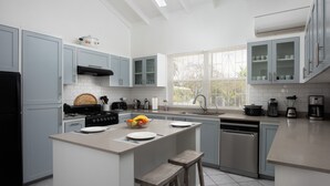 A modern kitchen with light blue cabinets, a central island with stools, a stove, and various appliances.