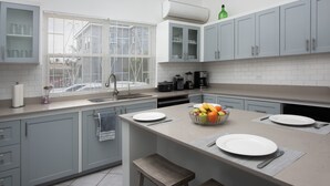 A modern kitchen with grey cabinets, a large window with blinds, a coffee maker, and a fruit bowl on the counter.