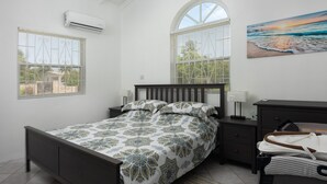 A bedroom with a bed, a dresser, a nightstand, and two windows with blinds.