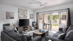 A modern living room with a flat-screen TV, grey sofas, a wooden coffee table, and artwork on the walls.