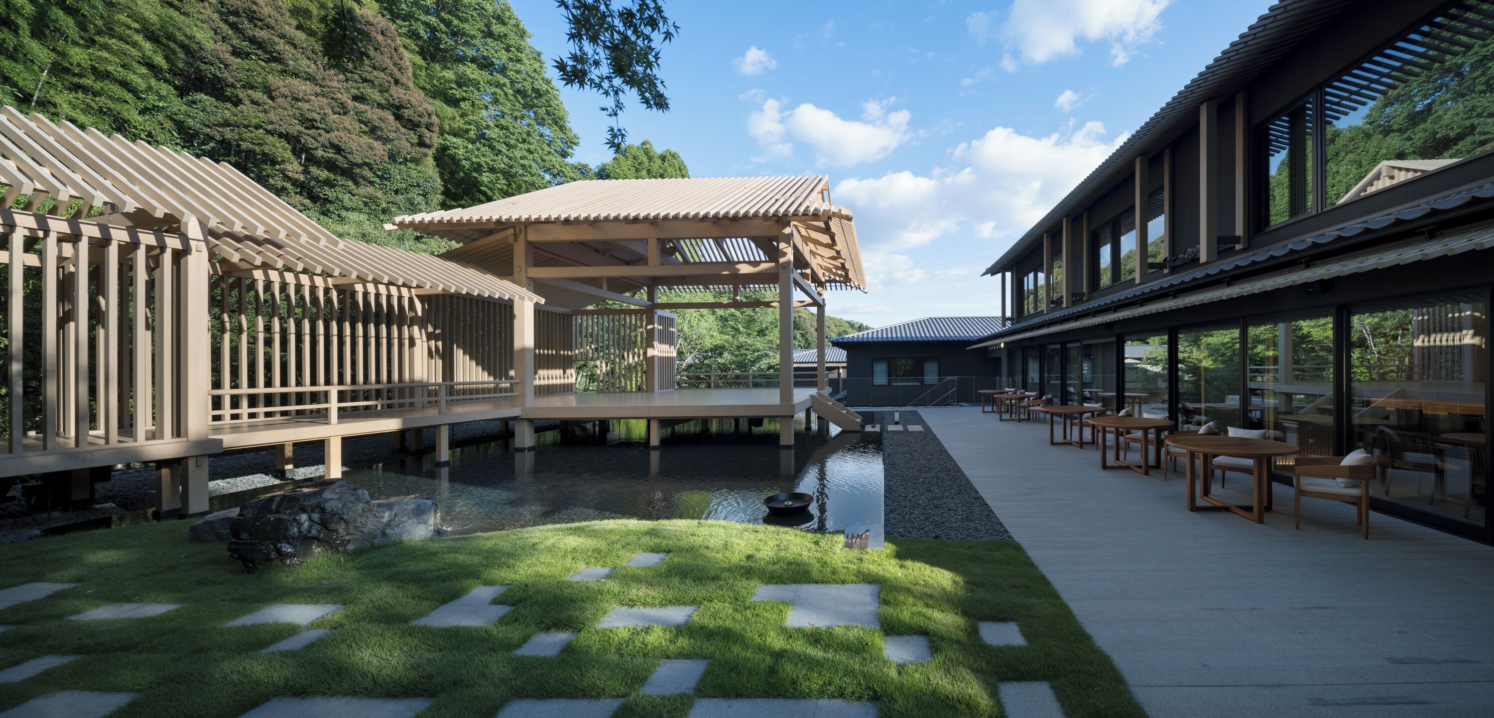 A modern outdoor area with a wooden deck, a small pond, and seating arrangements.