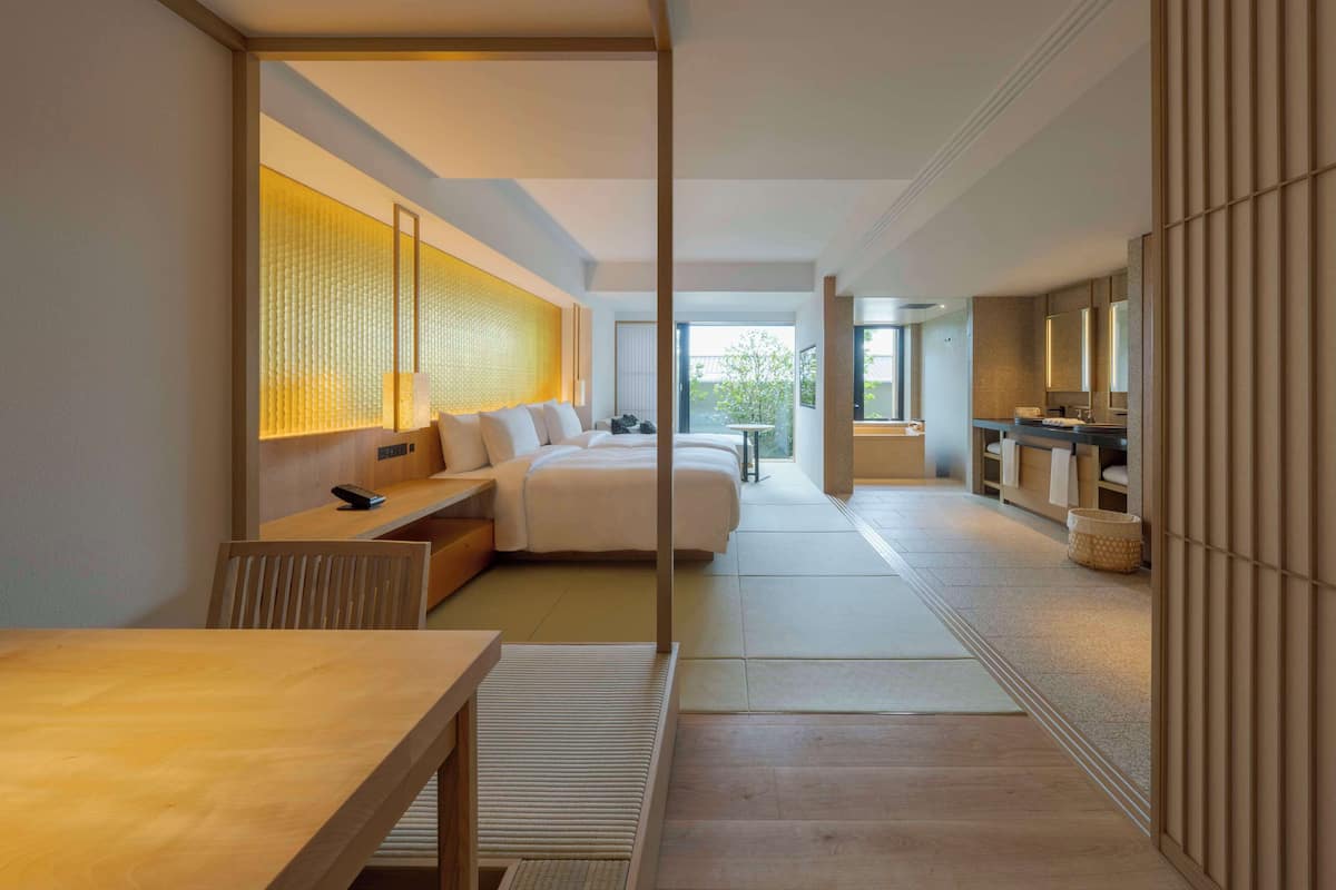 A modern hotel room with a large bed, a desk, a sitting area, and a bathroom with a bathtub and sink.