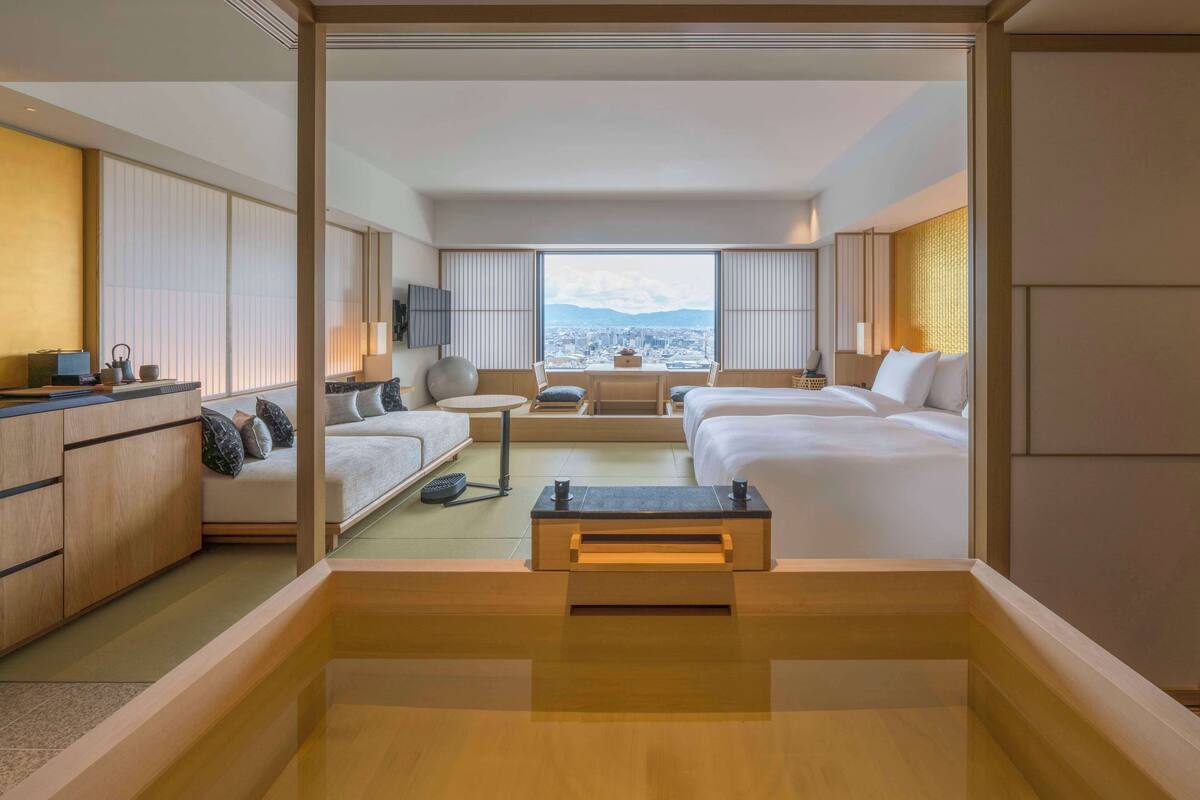 A modern hotel room with a sofa, a small table, a bed, and a view of a cityscape.