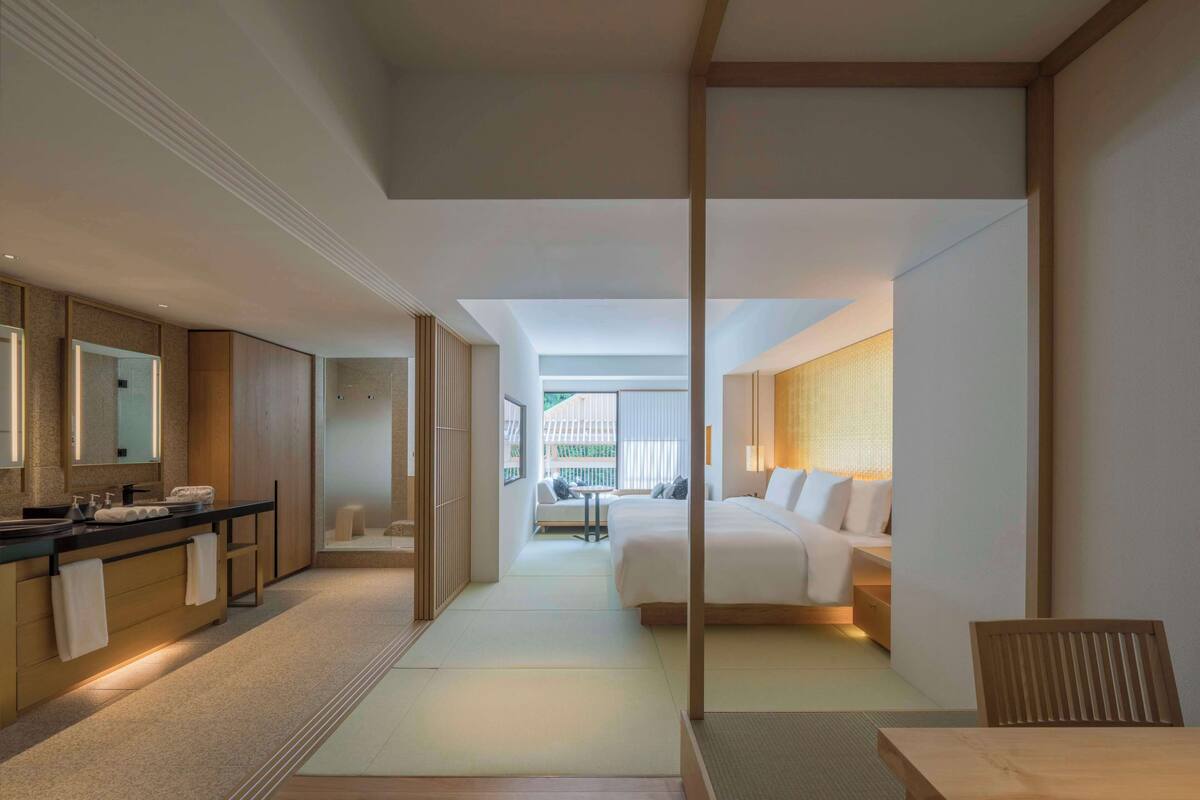A modern hotel room with a large bed, a desk, and a bathroom with a large mirror.