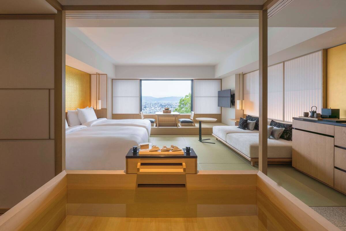 A modern hotel room with a bed, a desk, a sofa, and a view of the city.