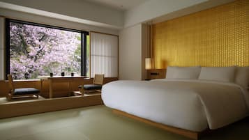 Una habitación de hotel moderna con una cama grande, un escritorio de madera y vistas a los cerezos en flor a través de un amplio ventanal.