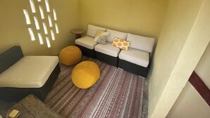 Une pièce chaleureuse avec un canapé, deux petits poufs ronds en osier, une petite table ronde et un tapis à motifs.