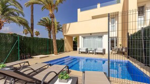 A modern pool area with lounge chairs and a table, surrounded by a fence and palm trees. - Cozy home in Cartagena (Cartagena)
