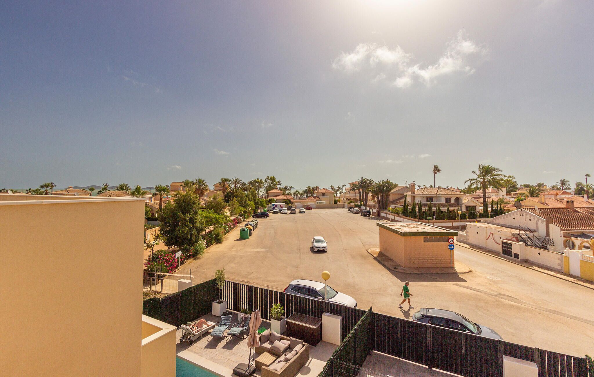 Zona residencial con cielo despejado, palmeras y una calle con coches estacionados.
